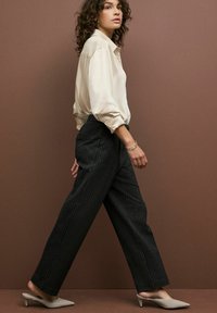 Beige Satinbluse mit Ballonärmeln, kombiniert mit schwarzen gestreiften, weit geschnittenen Hosen und grauen spitzen Mules. Minimalistisches goldenes Armband.