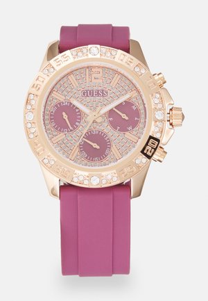 Rose gold watch with a pink silicone band, crystal accents, and a textured dial featuring three smaller sub-dials and a date display.