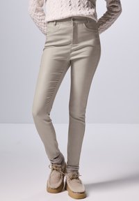 Beige stretchbroek met een aansluitend ontwerp, middelhoge taille en standaardzakken, gecombineerd met gestructureerde grijze sokken en beige fluffy schoenen.