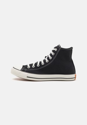 Baskets montantes en toile noire avec embout en caoutchouc blanc, lacets blancs et semelle blanche comportant une bande noire et un détail orange au talon.