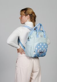 Mochila azul clara con patrón zigzag, lunares y un estampado del personaje Stitch. Cuenta con asas dobles y correas de hombro ajustables.