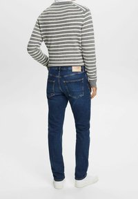 Pull rayé gris avec poignets côtelés, associé à un jean slim bleu foncé avec poches arrière. Des baskets blanches complètent la tenue.