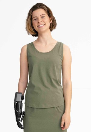 Olivgrünes ärmelloses Baumwolltop mit rundem Ausschnitt, kombiniert mit einem passenden Rock. Der linke Arm hat eine schwarze robotische Prothese.