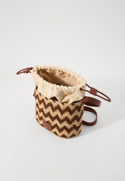 Μικρή καφετιά και μπεζ πλεκτή τσάντα χιαστί με ζικ-ζακ σχέδιο και μπεζ υφασμάτινο κορδόνι κλεισίματος σε απλό φόντο.