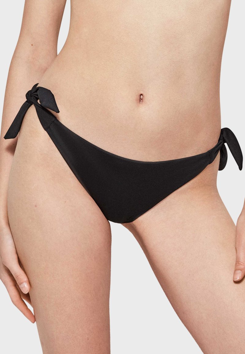 Parte inferior de bikini negra con una textura suave y un diseño de corte bajo. Presenta dos lazos en cada lado para un ajuste ajustable.