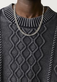 Pull en maille grise avec un motif en losange texturé et un col côtelé. Un collier en chaîne argentée est visible autour du cou.