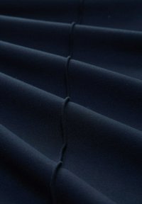 Tessuto blu navy con una superficie liscia, caratterizzato da strati piegati e dettagli di cucitura sottili, creando un aspetto pulito e strutturato.