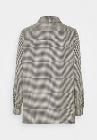 Svartvit houndstooth-mönstrad skjorta med krage, långa ärmar med knäppte manschetter och rak fåll.
