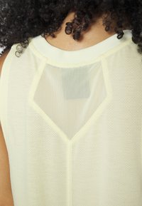 Top sin mangas de color amarillo claro con un inserto de malla en la espalda en forma de diamante, con una textura suave y transpirable y un cuello redondeado.