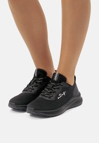 Zapatillas deportivas negras con parte superior de malla, cordones reflectantes y un cuello acolchado. Cuentan con una suela texturizada para un buen agarre y comodidad.