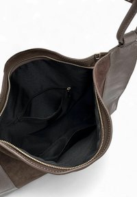 Sac à main en cuir marron avec intérieur en tissu noir, montrant une poche zippée ouverte et un compartiment principal spacieux sur un fond blanc.
