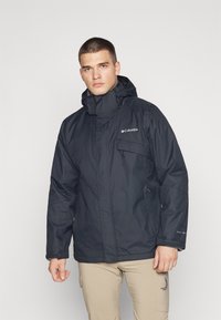 Black waterproof jacket with a hood, featuring a zip front, elastic cuffs, and a branded patch on the chest. Smooth fabric texture.
