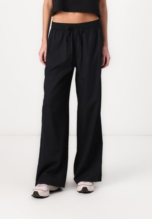 Black wide-leg pants with an elastic waistband and drawstring. Smooth fabric texture. Paired with light pink sneakers.