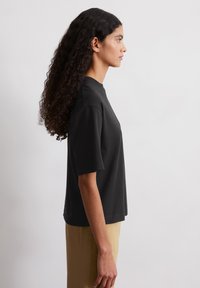 T-shirt nera a maniche corte con colletto alto, realizzata in cotone morbido. La vestibilità è rilassata, con cuciture visibili lungo i bordi.