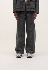 Wide-leg, gray denim pants with a subtle floral pattern. The material appears sturdy, with a casual fit. Worn with shiny silver sneakers.
