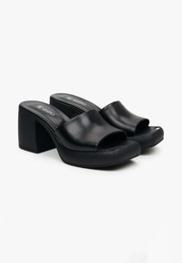 Zwarte blokhak mules met een open teen en een brede bovenband. Gemaakt van soepel leer met een lichte glanzende afwerking.