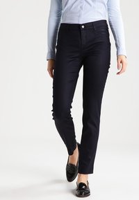 Dark blue, slim-fit trousers with a smooth texture, five pockets, and a button closure. Worn with a light blue shirt and black loafers.