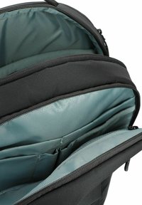Zwarte rugzakinterieur met een gladde teal voering, met rits afgesloten compartimenten en gevoerde secties voor organisatie. Materiaal lijkt duurzaam.
