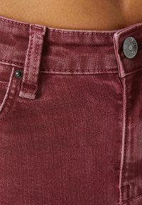 Burgundy denimjeans med en texturerad yta, som har knäppning, kontrasterande sömmar och en något urblekt look.