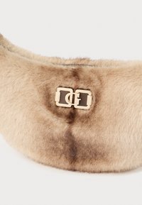 Tas van nepbont in beige met een zachte textuur, voorzien van een dubbele gesp in goudkleur en een gebogen, compact profiel.