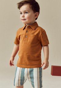 Oranger Poloshirt mit kurzen Ärmeln und einer Brusttasche; gemusterte Shorts in blau, weiß und braunen Streifen; glatte Textur.