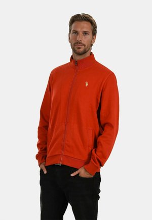 Red zip-up jacket made from soft fabric, featuring a high collar, front pockets, and a gold logo accent on the left chest.