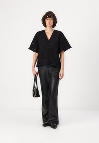 Black embroidered top with a V-neck and wide sleeves, paired with black leather trousers and a small black bag. Smooth texture overall.