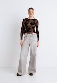 Μαύρο τοπ μακρυμάνικο από διχτυωτό ύφασμα με ανθισμένο σχέδιο, συνδυασμένο με ανοιχτό γκρι παντελόνι με φαρδιά πόδια. Η εμφάνιση έχει άνετη εφαρμογή και ουδέτερα χρώματα.