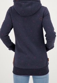 Sudadera de color azul oscuro con motas rosas, tejido texturizado, mangas largas y capucha con cordón. Presenta un parche de cuero en el lado inferior.