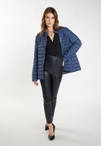 Giacca trapuntata puffer navy, con colletto alto e zip, abbinata a pantaloni in pelle neri a vita alta e tacchi neri.