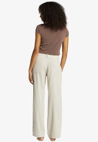 Chemise brune, ajustée, à manches courtes, associée à un pantalon large beige clair en ripstop avec poches arrière et tissu texturé.
