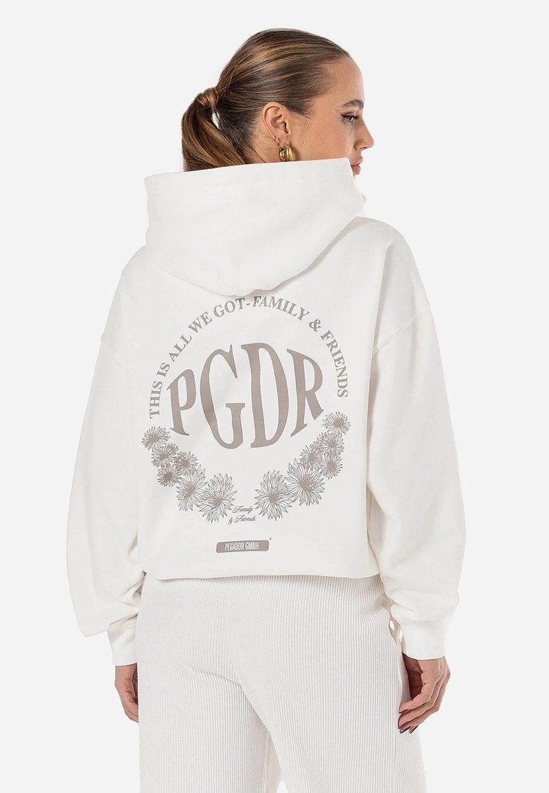 Fehér, puha anyagból készült cropped kapucnis pulóver, nagyméretű bézs grafikával, amely virágokat és "PGDR" feliratot tartalmaz a hátsó részén.