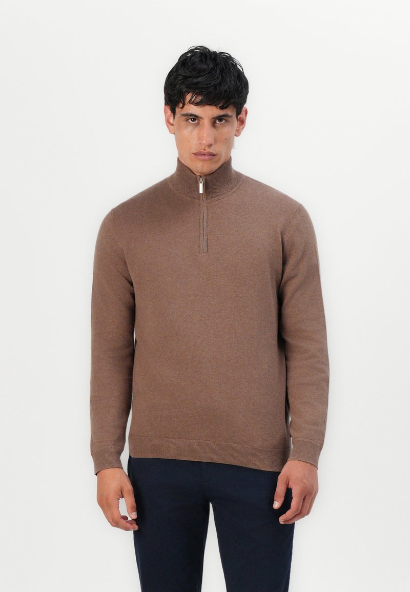 Hnědý svetr na zip s vysokým límcem, vyrobený z měkké látky. Design zahrnuje žebrované manžety a lem a stříbrný zip.