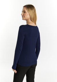 Marineblauwe sweater met lange mouwen, die een textured breigarenontwerp toont, met decoratieve accenten op de schouders en een ronde halslijn.