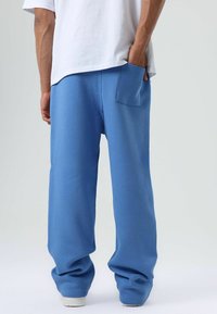 Blauwe trainingsbroek gemaakt van zacht materiaal, met een achterzak, losse pasvorm en geribbelde boorden bij de enkels. Eenvoudig ontwerp zonder patronen.