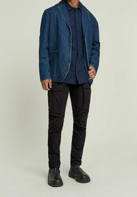 Denim blazer in dark blue with a notched collar and front pockets, paired with black cargo pants featuring multiple pockets and sturdy black boots.