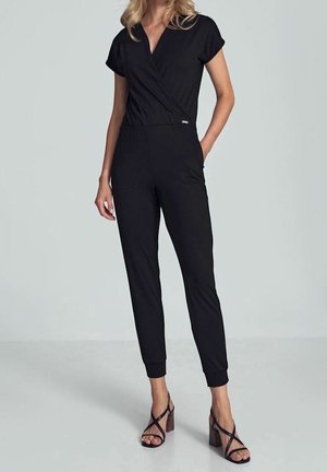 Combinaison noire à manches courtes, devant croisé, taille élastique, jambes fuselées et texture lisse. Associée à des sandales à talons à brides.