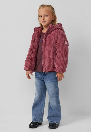 Pluchen, geribbelde, bordeauxrode pufferjack met een capuchon, gecombineerd met een donker T-shirt en lichtblauwe flare jeans; zwarte schoenen.