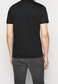 Polo noir à manches courtes avec un motif texturé de palmiers. Confectionné en tissu doux, il présente un col classique et des fentes latérales.