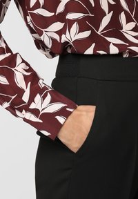 Långärmad skjorta i bordeauxfärgad tyg med vita bladmönster, kombinerad med svarta byxor som har sidoficka och texturerad midjeband.