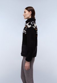 Giacca in pile nera con accenti bianchi, arancioni e grigi a fantasia, colletto alto e chiusura con zip. Pannello inferiore nero liscio, texture caldo.