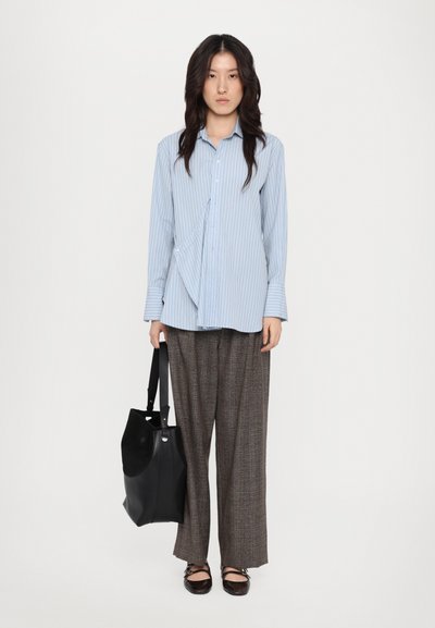 Chemise à rayures bleu clair, pantalon large à carreaux gris, sac fourre-tout noir et chaussures plates noires. Tissu lisse avec une coupe ajustée.