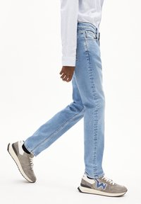  Lichtblauwe denim jeans met een rechte pasvorm, gecombineerd met grijze en witte sneakers met blauwe accenten en een gestructureerde afwerking.