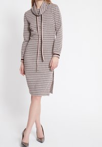 Robe à manches longues en motif vichy rose et noir, avec un col drapé, une finition contrastée aux poignets et des fentes latérales.