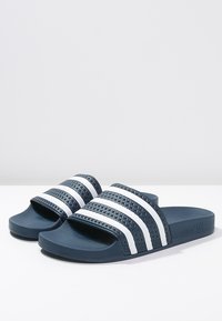 Marinblåa slide-sandaler med en texturerad rem och tre vita ränder. Mjuk gummisula med platt design för avslappnad användning.