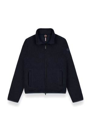 Marineblå ribstrikket jakke med høj krave, frontlynlås og to sidelommer. Har et logo-patch på venstre ærme, struktureret stof.