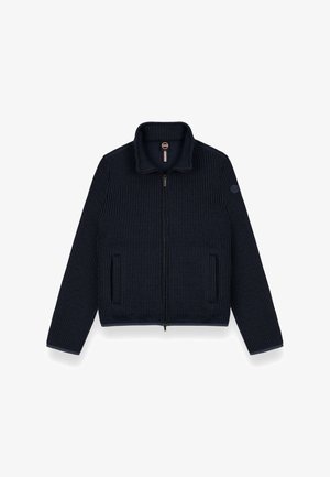 Laivastonsininen ribattu neuletakki, jossa on korkea kaulus, edessä vetoketju ja kaksi sivutaskua. Vasemmassa hihassa on logopatch, teksturoitu kangas.