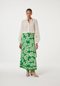 Witte blouse met opgestoken mouwen en kanten accenten, gecombineerd met een groene rok met bloemenpatroon met blauwe en gele details. Crème enkellaarsjes.