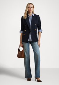 Marineblå dobbelspent blazer med gullknapper, stripet skjorte, lyseblå vide jeans, brun skinnveske og brune høye hæler.