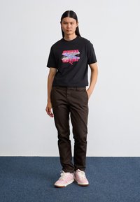 Sort t-shirt med farverig grafisk print, brune bukser og lyserøde sneakers. Oplevelsen har en afslappet pasform og casual design elementer.
